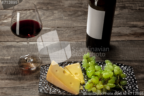 Image of A bottle and a glass of red wine with fruits over wooden background