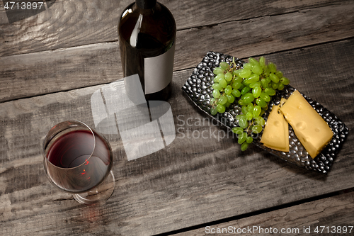 Image of A bottle and a glass of red wine with fruits over wooden background