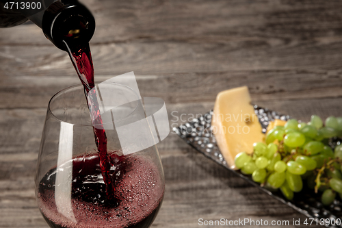 Image of A bottle and a glass of red wine with fruits over wooden background