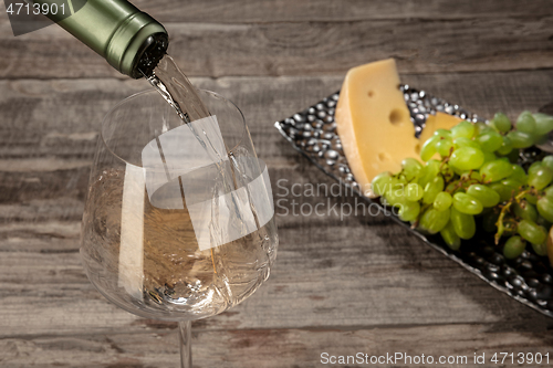 Image of A bottle and a glass of white wine with fruits over wooden background