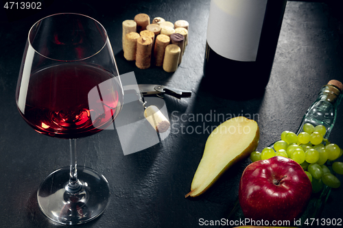 Image of A bottle and a glass of red wine with fruits over dark stone background