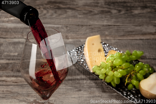 Image of A bottle and a glass of red wine with fruits over wooden background