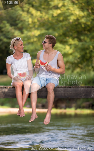 Image of couple enjoying watermelon while sitting on the wooden bridge