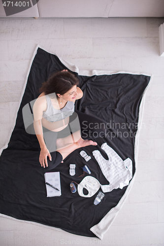 Image of top view of pregnant woman checking list of baby clothes