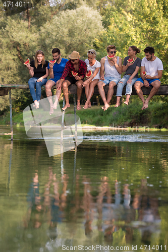 Image of friends enjoying watermelon while sitting on the wooden bridge