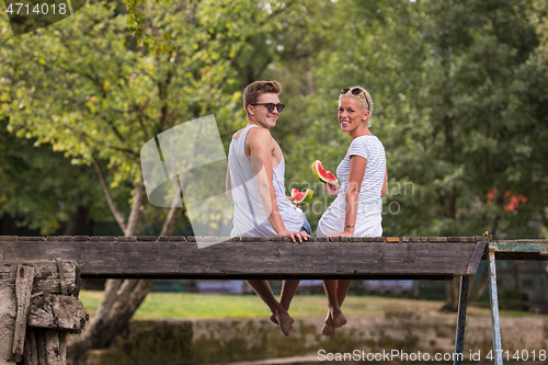 Image of couple enjoying watermelon while sitting on the wooden bridge