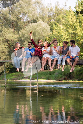 Image of friends enjoying watermelon while sitting on the wooden bridge