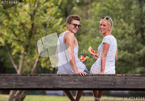 Image of couple enjoying watermelon while sitting on the wooden bridge