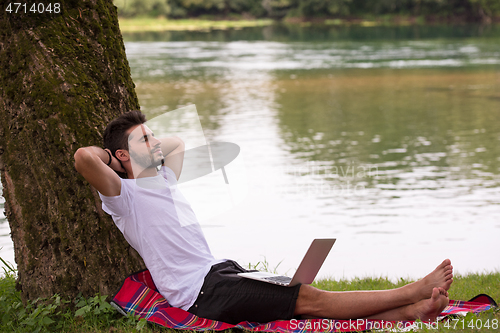 Image of man using a laptop computer on the bank of the river