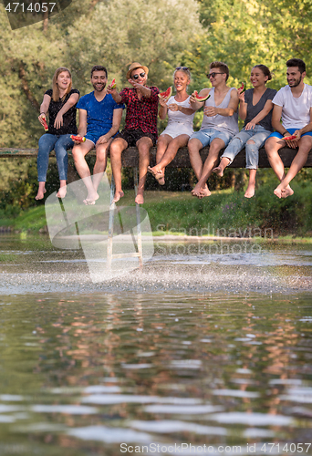 Image of friends enjoying watermelon while sitting on the wooden bridge
