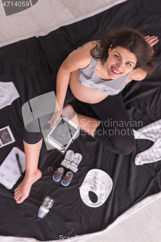 Image of top view of pregnant woman checking list of baby clothes