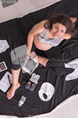 Image of top view of pregnant woman checking list of baby clothes