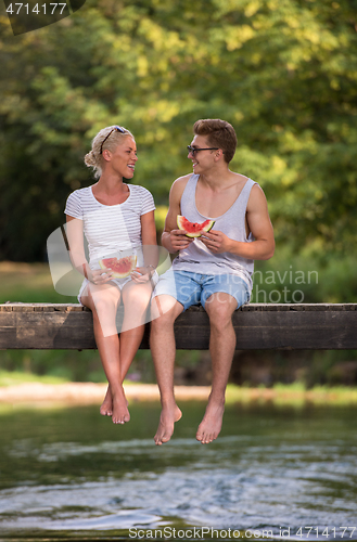 Image of couple enjoying watermelon while sitting on the wooden bridge