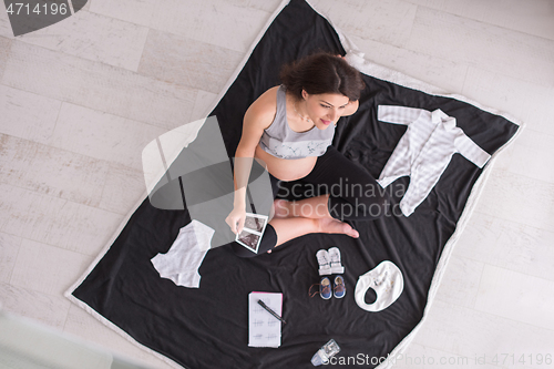 Image of top view of pregnant woman checking list of baby clothes