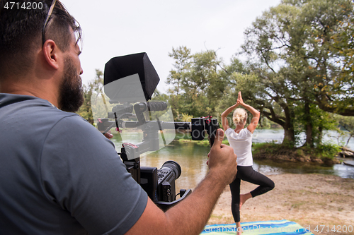 Image of young videographer recording while woman doing yoga exercise