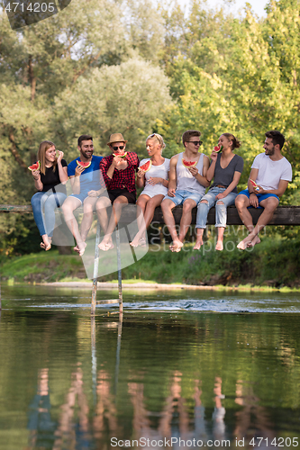 Image of friends enjoying watermelon while sitting on the wooden bridge