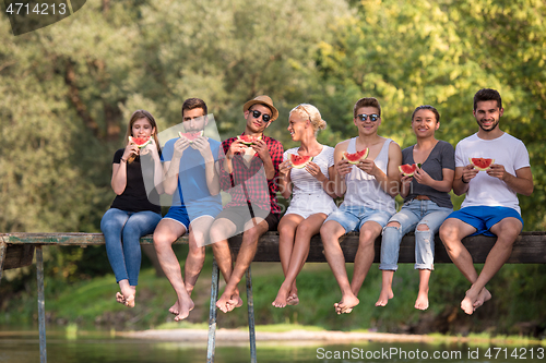 Image of friends enjoying watermelon while sitting on the wooden bridge
