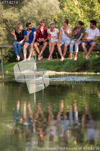 Image of friends enjoying watermelon while sitting on the wooden bridge