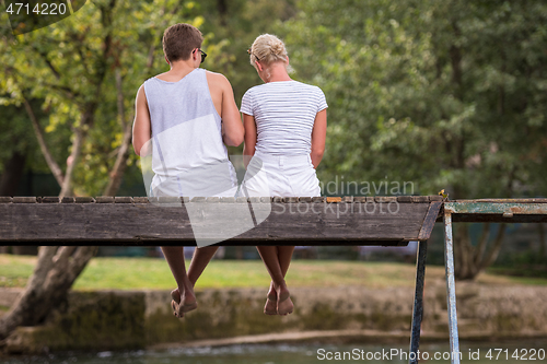 Image of couple enjoying watermelon while sitting on the wooden bridge