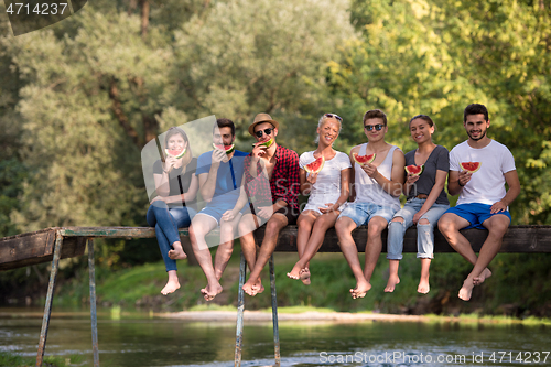 Image of friends enjoying watermelon while sitting on the wooden bridge