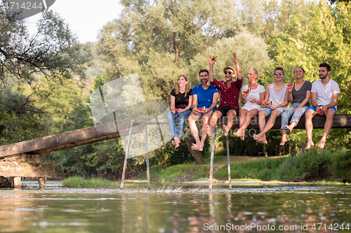Image of friends enjoying watermelon while sitting on the wooden bridge