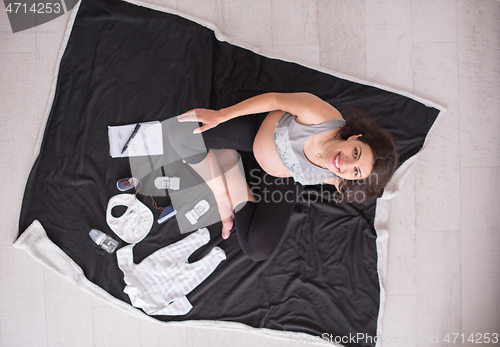 Image of top view of pregnant woman checking list of baby clothes