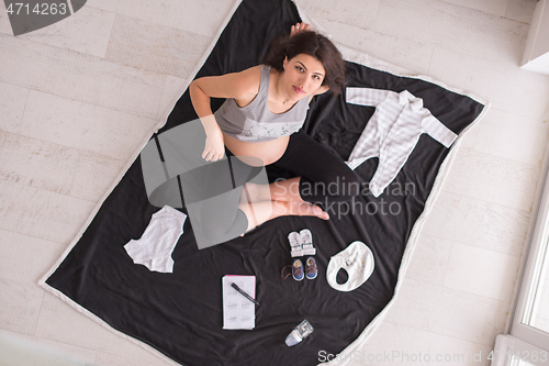 Image of top view of pregnant woman checking list of baby clothes