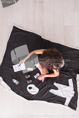 Image of top view of pregnant woman checking list of baby clothes
