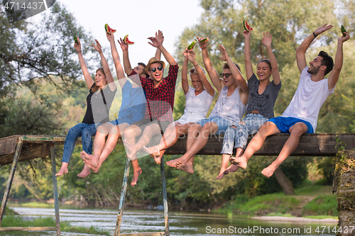 Image of friends enjoying watermelon while sitting on the wooden bridge