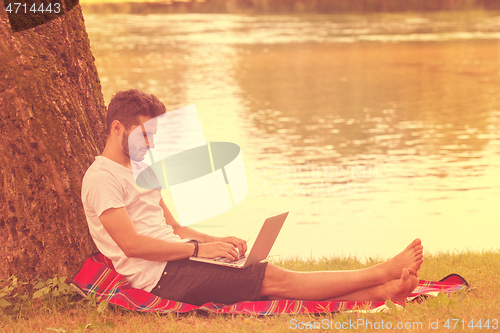 Image of man using a laptop computer on the bank of the river