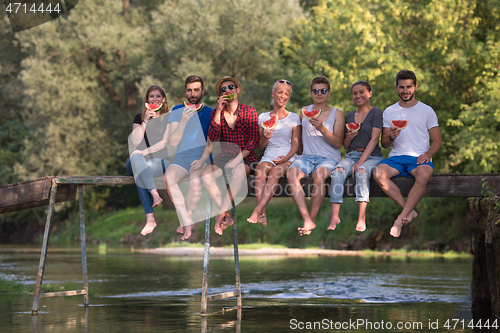 Image of friends enjoying watermelon while sitting on the wooden bridge