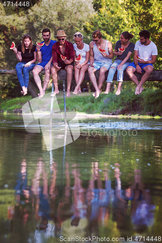 Image of friends enjoying watermelon while sitting on the wooden bridge