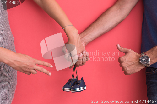 Image of young pregnant couple holding newborn baby shoes