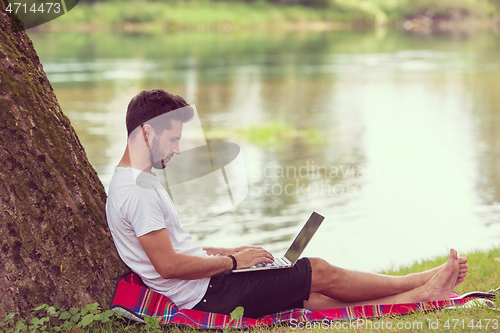 Image of man using a laptop computer on the bank of the river