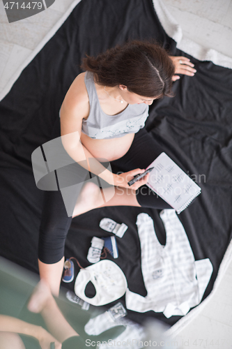 Image of top view of pregnant woman checking list of baby clothes