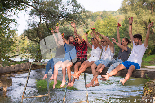 Image of friends enjoying watermelon while sitting on the wooden bridge