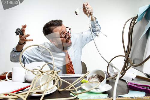 Image of Young man tangled in wires on the workplace