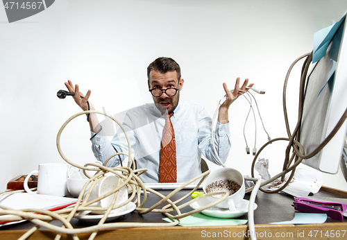 Image of Young man tangled in wires on the workplace