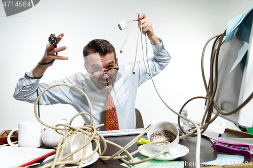 Image of Young man tangled in wires on the workplace