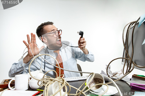 Image of Young man tangled in wires on the workplace