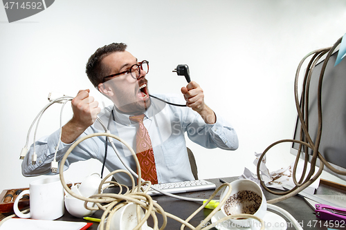 Image of Young man tangled in wires on the workplace