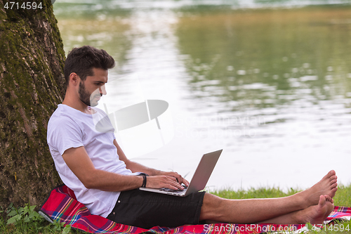 Image of man using a laptop computer on the bank of the river