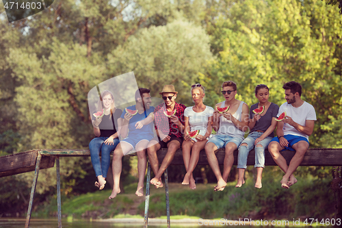 Image of friends enjoying watermelon while sitting on the wooden bridge