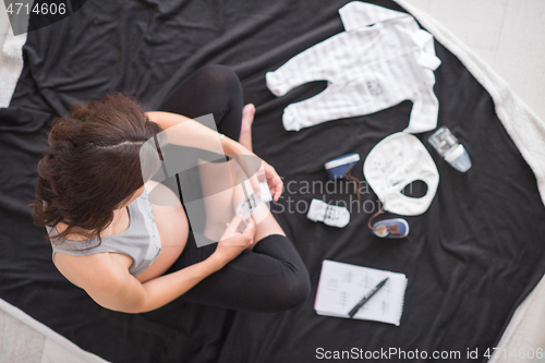 Image of top view of pregnant woman checking list of baby clothes