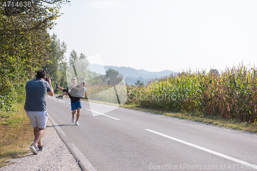 Image of videographer recording while couple jogging along a country road