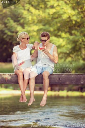 Image of couple enjoying watermelon while sitting on the wooden bridge