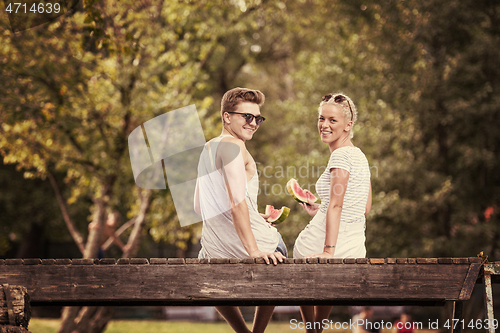 Image of couple enjoying watermelon while sitting on the wooden bridge