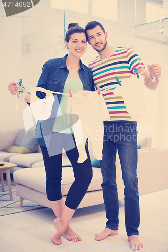 Image of young couple holding baby bodysuits at home