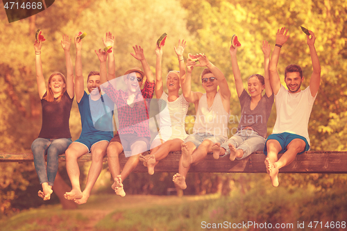 Image of friends enjoying watermelon while sitting on the wooden bridge