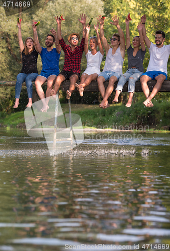 Image of friends enjoying watermelon while sitting on the wooden bridge